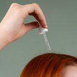 close-up-of-hand-applying-hair-serum-on-red-hair-with-a-drop